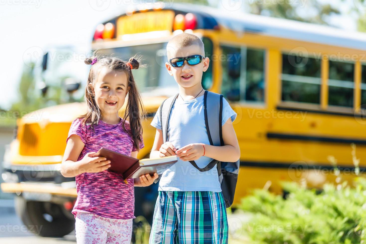 Laughing smiling Caucasian boy student kid with funny face expression walking near yellow bus on 1 September day. Education and back to school concept. Child pupil ready to learn and study. photo