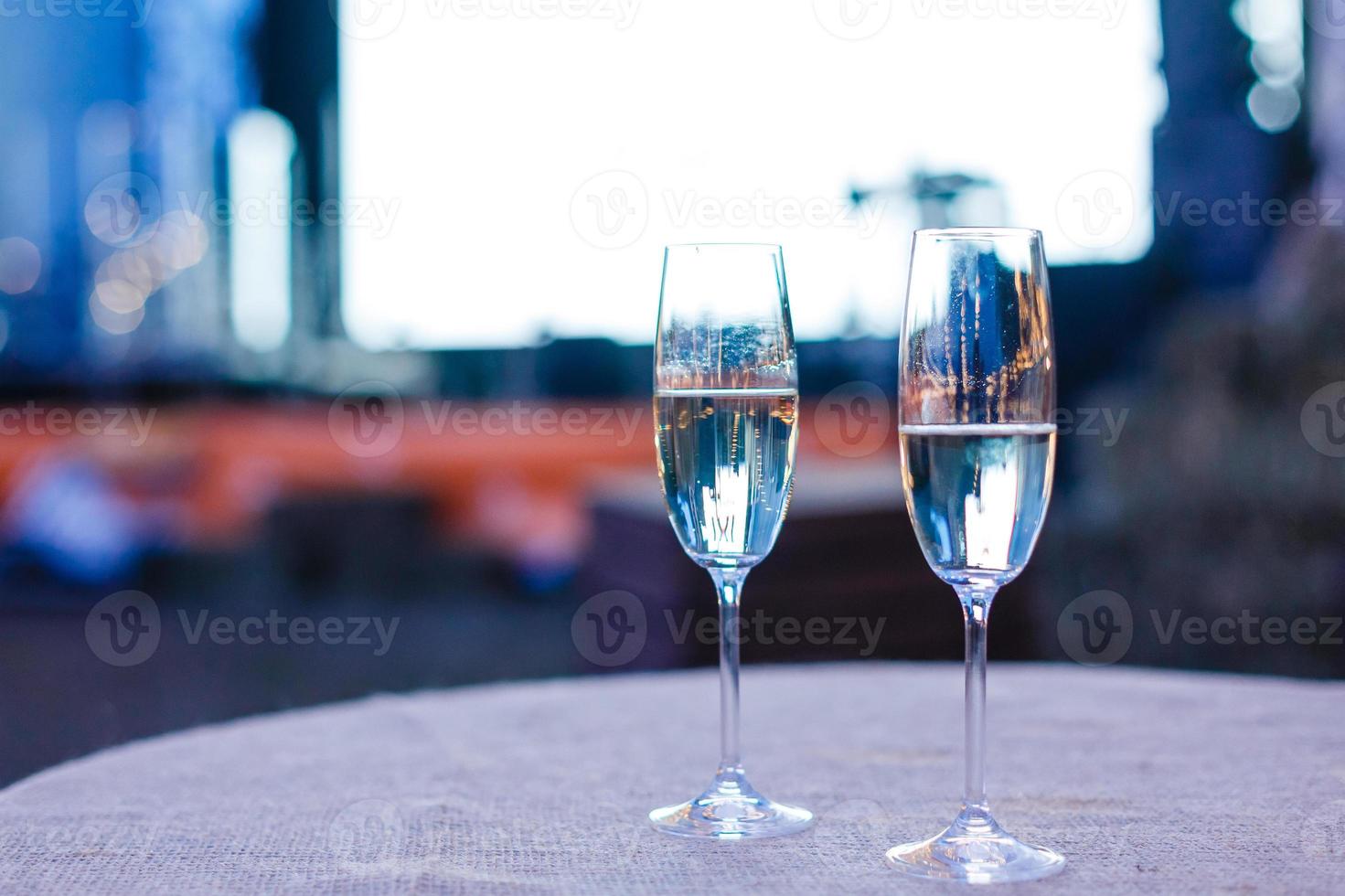 photo of two champagner glasses on glass table with bokeh background