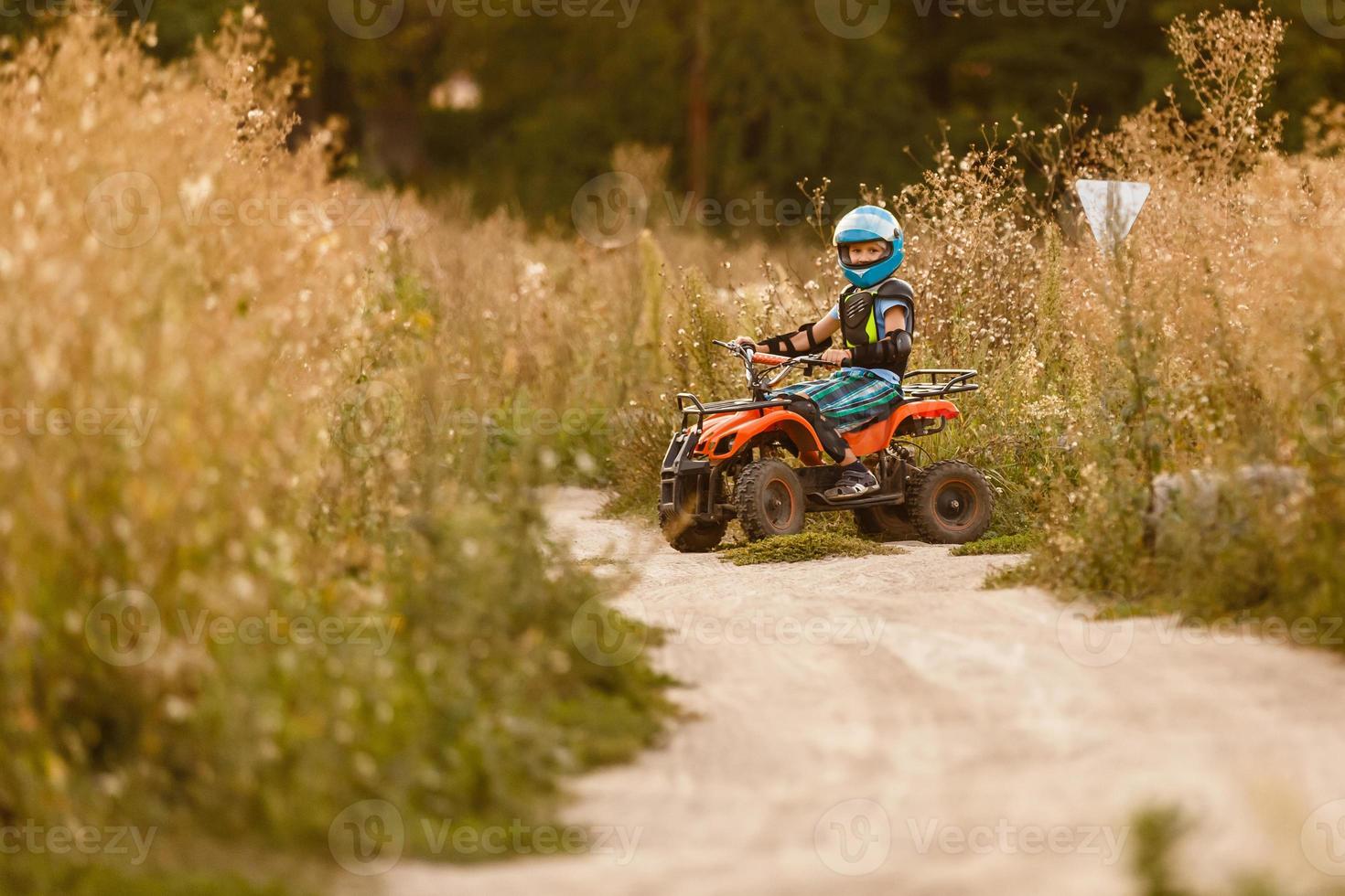 A little boy wearing a helmet riding a quad bike on the shore of a mountain river. photo