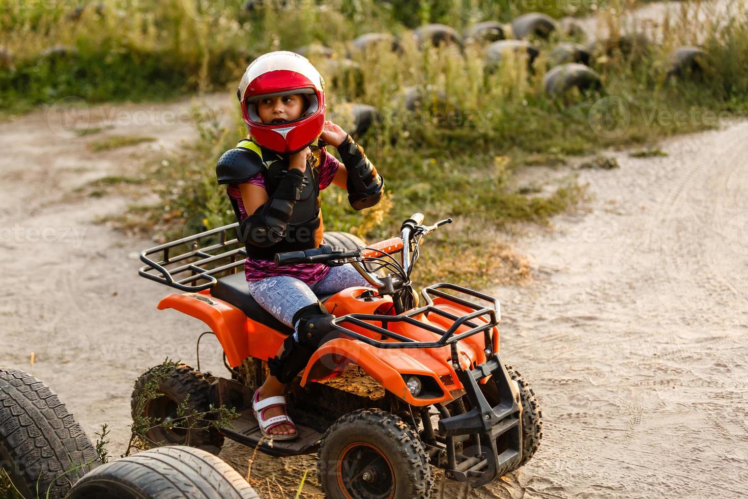 la niña monta un quad atv. una mini quad es una chica genial con casco y ropa protectora. El coche eléctrico de quad eléctrico para niños populariza la tecnología ecológica. foto