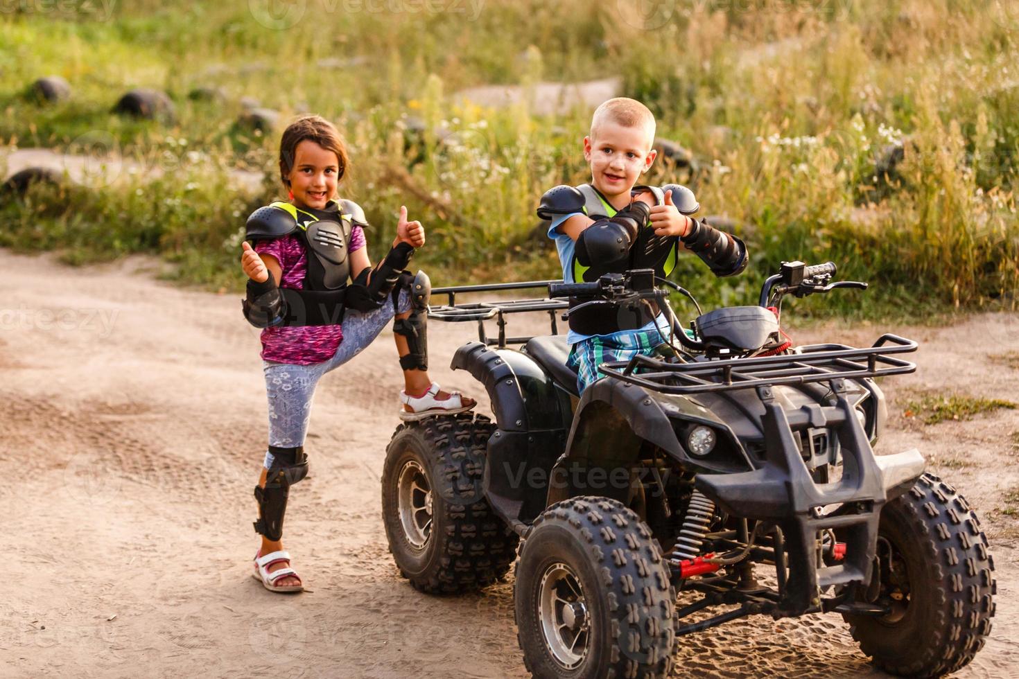 Happy little children playing on road at the day time. They driving on quad bike in the park. Kids having fun on the nature. Concept of happiness. photo