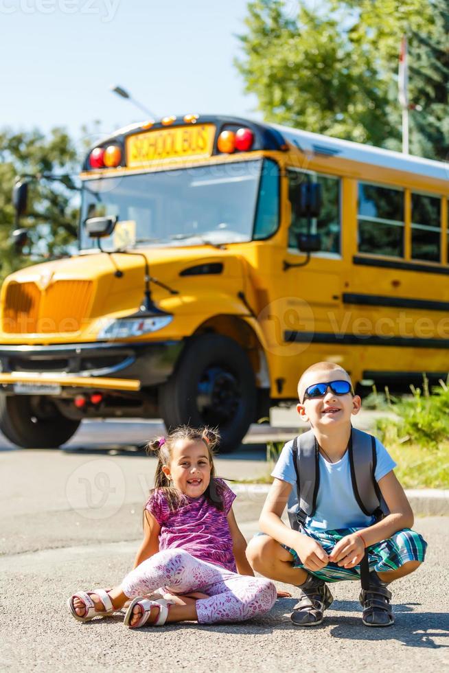 Laughing smiling Caucasian boy student kid with funny face expression walking near yellow bus on 1 September day. Education and back to school concept. Child pupil ready to learn and study. photo