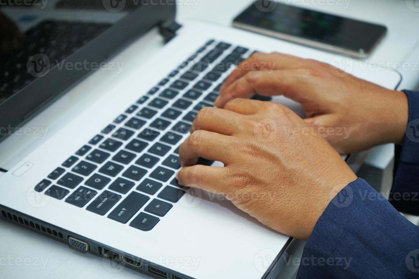 hombre de negocios asiático manos trabajando en la oficina con computadora portátil y teléfono móvil, escribiendo en el teclado en su escritorio, cerrar foto