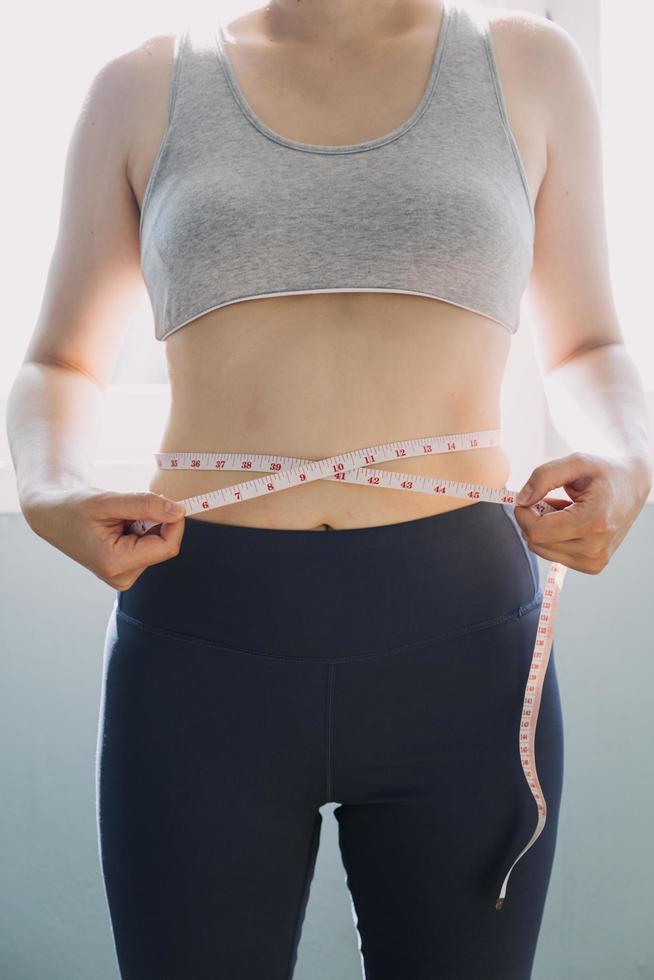 hermosa mujer gorda con cinta métrica usa su mano para exprimir el exceso de grasa que está aislado en un fondo blanco. ella quiere perder peso, el concepto de cirugía y descomponer grasa bajo el foto