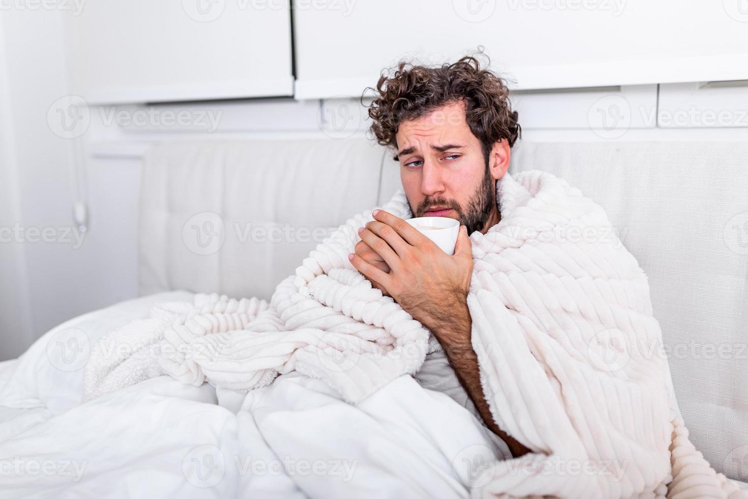 Sick day at home. Handsome Man has fever and common cold. Cough. Closeup Of Young Man Caught Cold Or Flu Illness. Portrait Of Unhealthy man Feeling Pain In Throat and drinking hot beverage. photo