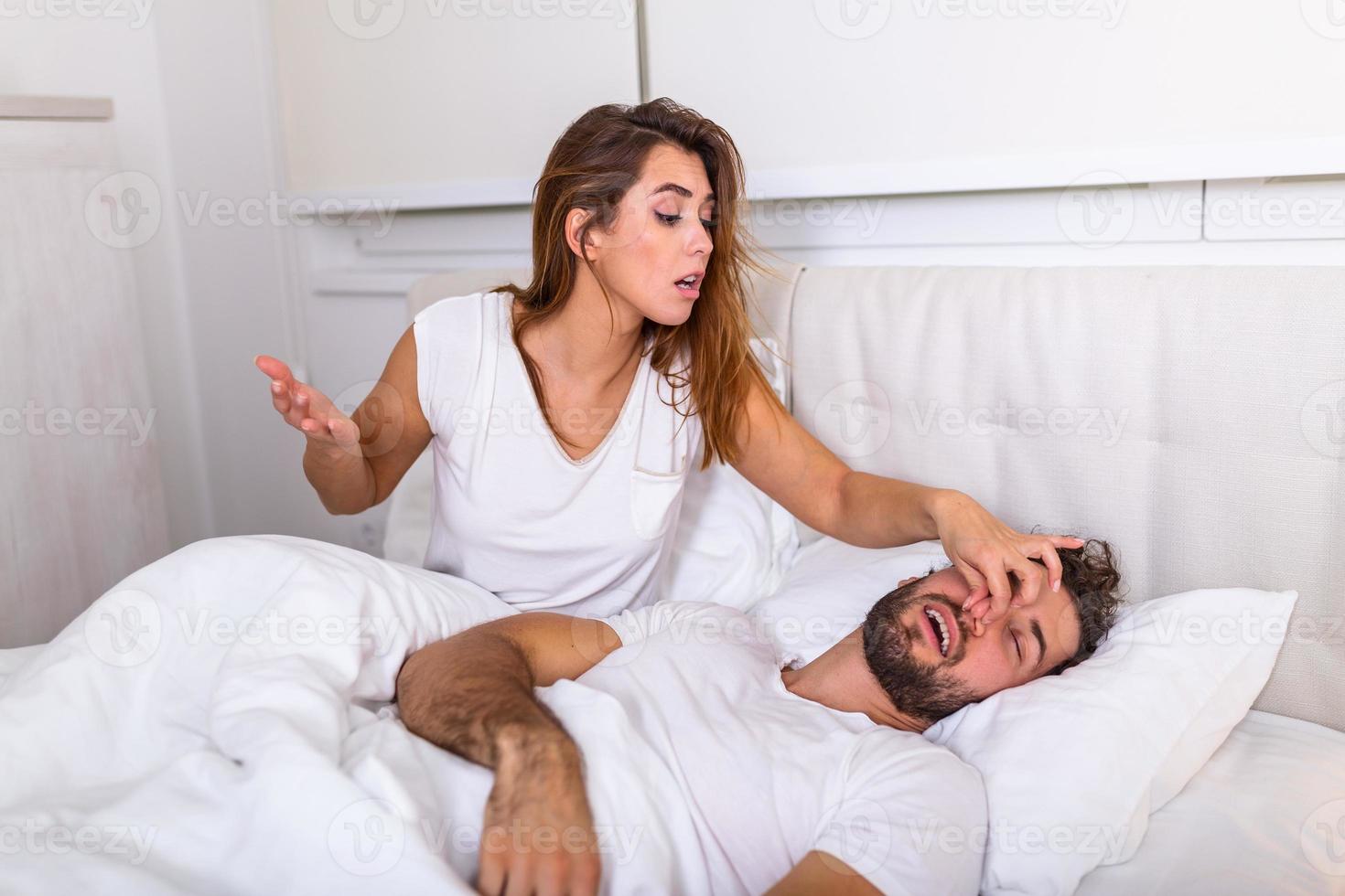 Couple in bed, man snoring and woman can't sleep. Snoring man and young woman. Couple sleeping in bed. Young girl can't sleep because of her man's snoring holding his nose. Snoring man problem photo