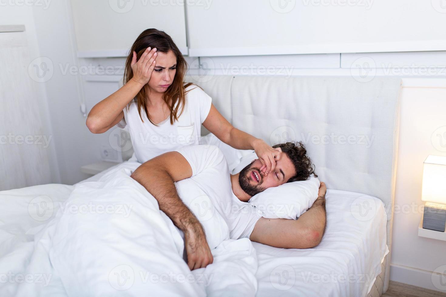 Couple in bed, man snoring and woman can't sleep. Snoring man and young woman. Couple sleeping in bed. Young girl can't sleep because of her man's snoring holding his nose. Snoring man problem photo