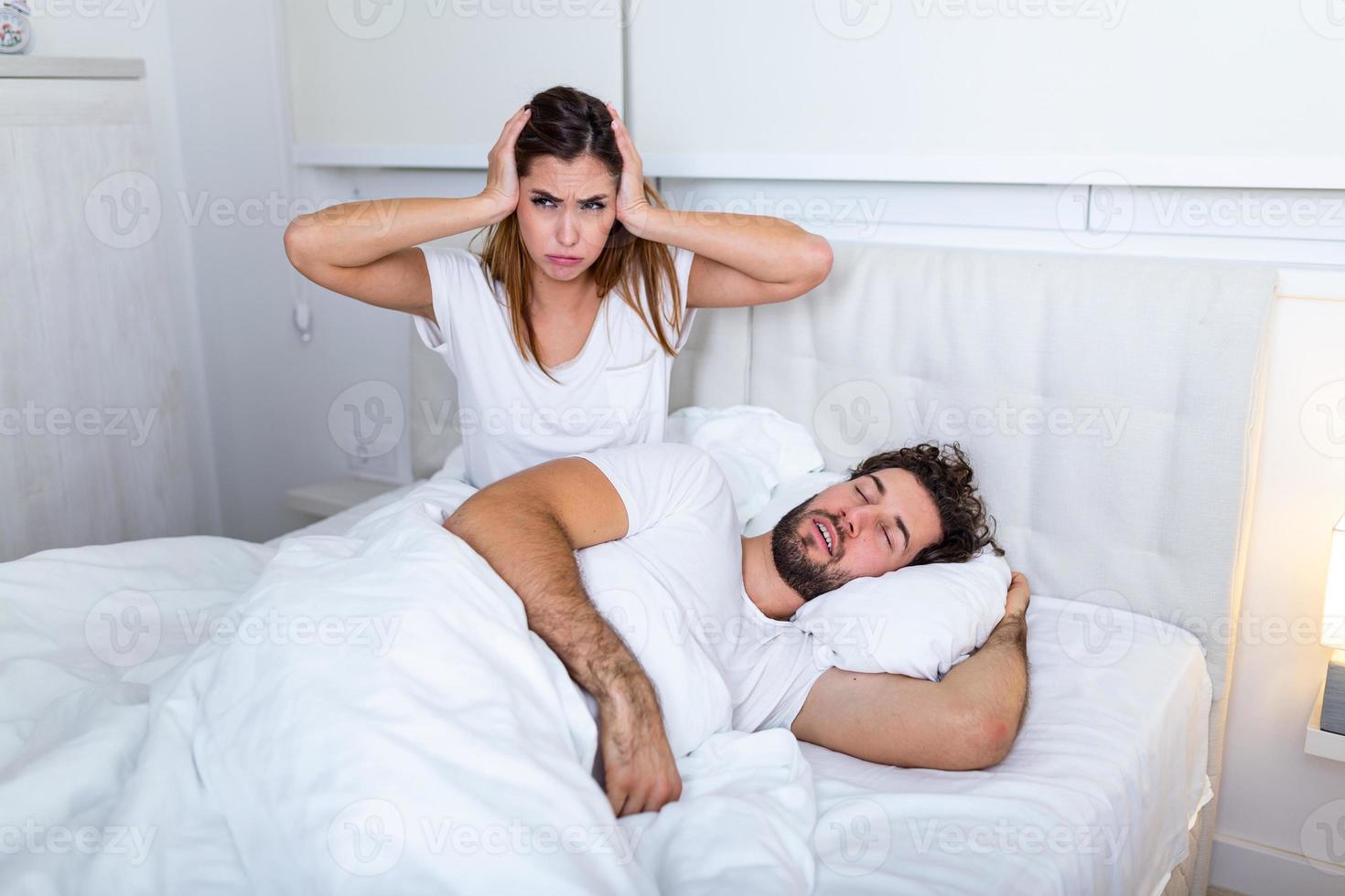 Snoring man. Couple in bed, man snoring and woman can not sleep. Picture of angry woman in bed with snoring man. Portrait of woman blocking ears with hands while man snoring on bed photo