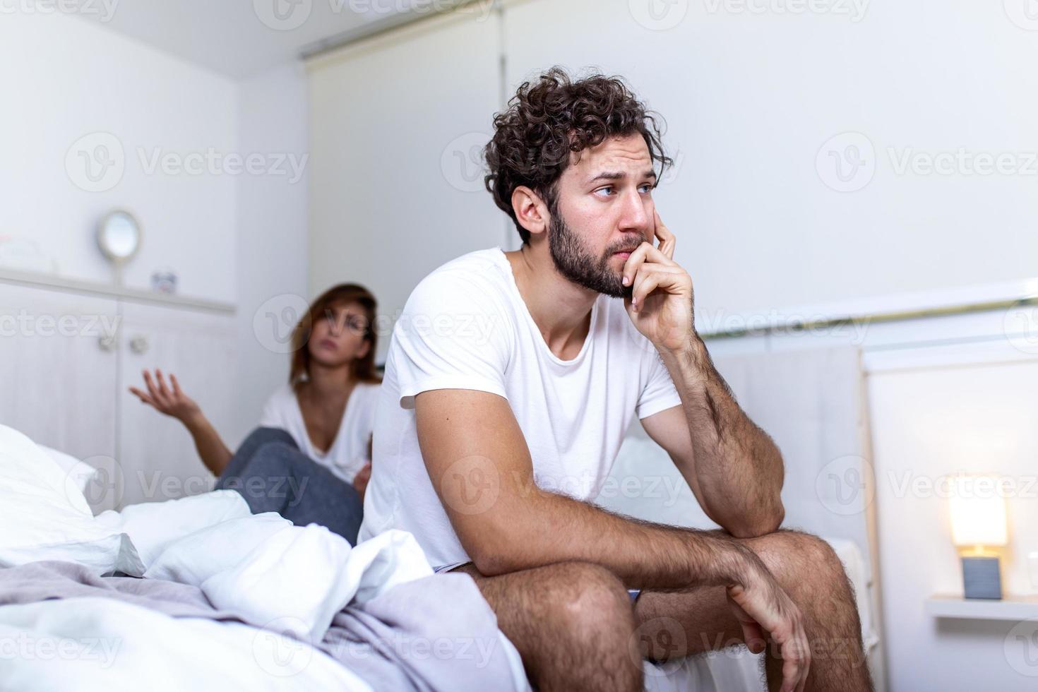 Beautiful girl and a frustrated man sitting in bed and not looking at each other. Upset couple ignoring each other. Worried man in tension at bed. Young couple angry with each other after a fight. photo