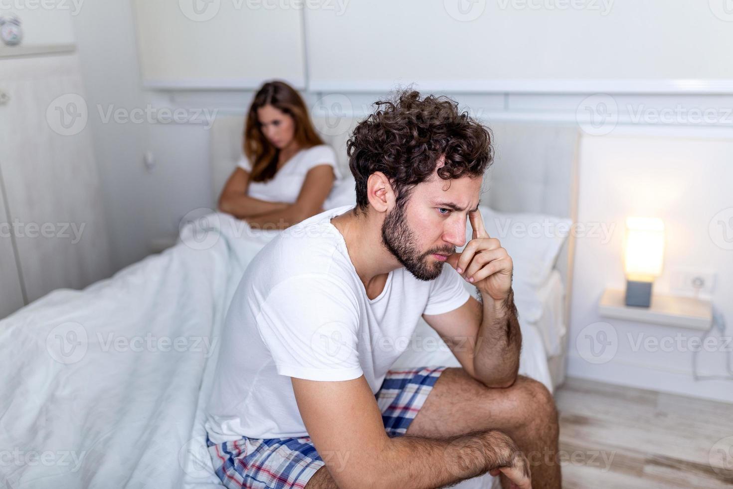 Beautiful girl and a frustrated man sitting in bed and not looking at each other. Upset couple ignoring each other. Worried man in tension at bed. Young couple angry with each other after a fight. photo
