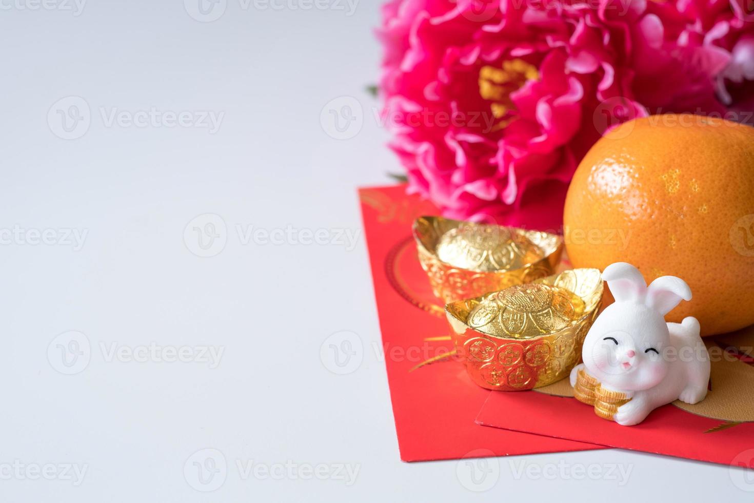 año nuevo chino del concepto del festival del conejo. naranja, sobres rojos, dos conejos y lingotes de oro decorados con flores de ciruela sobre fondo blanco. foto