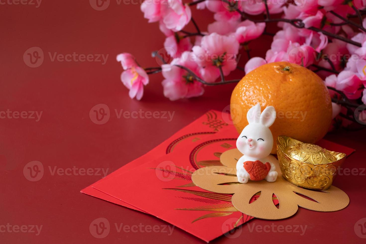 año nuevo chino del concepto del festival del conejo. naranja mandarina, sobres rojos, conejo y lingotes de oro decorados con flor de ciruela sobre fondo rojo. foto