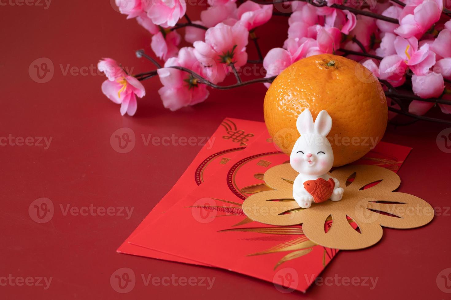 Chinese New Year of the rabbit festival concept. Mandarin orange, red envelopes, rabbit and gold ingot decorated with plum blossom on red background. photo