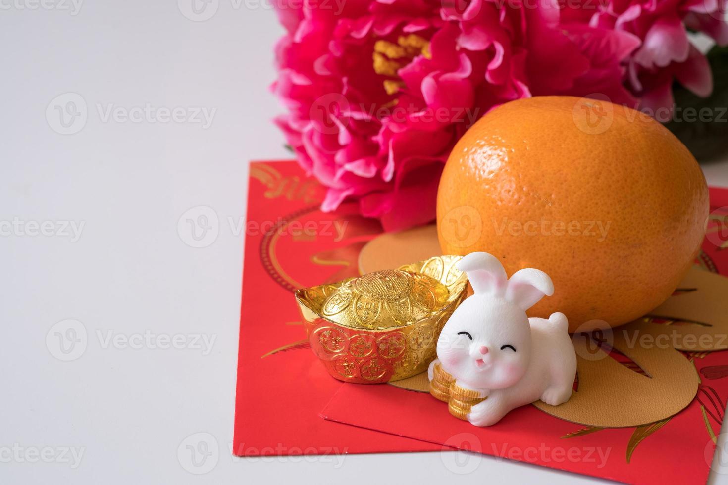 año nuevo chino del concepto del festival del conejo. naranja, sobres rojos, dos conejos y lingotes de oro decorados con flores de ciruela sobre fondo blanco. foto