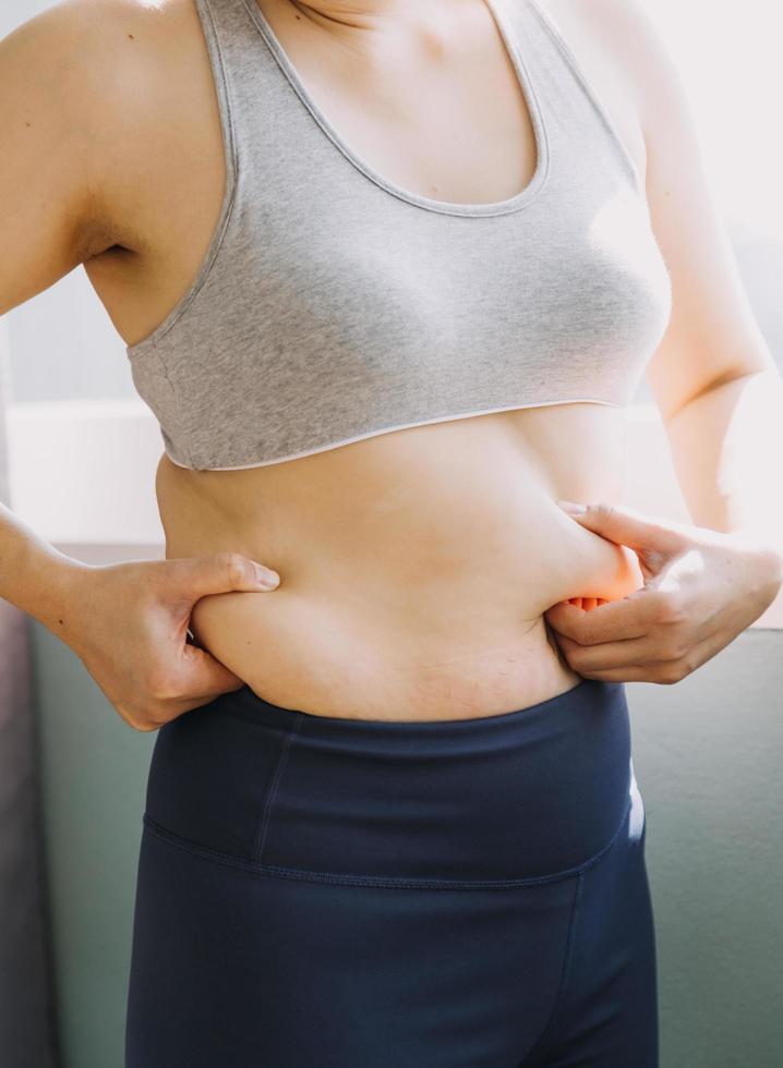 hermosa mujer gorda con cinta métrica usa su mano para exprimir el exceso de grasa que está aislado en un fondo blanco. ella quiere perder peso, el concepto de cirugía y descomponer grasa bajo el foto