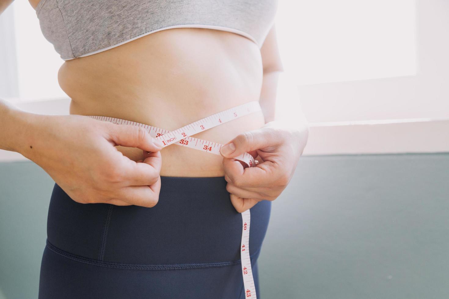 hermosa mujer gorda con cinta métrica usa su mano para exprimir el exceso de grasa que está aislado en un fondo blanco. ella quiere perder peso, el concepto de cirugía y descomponer grasa bajo el foto