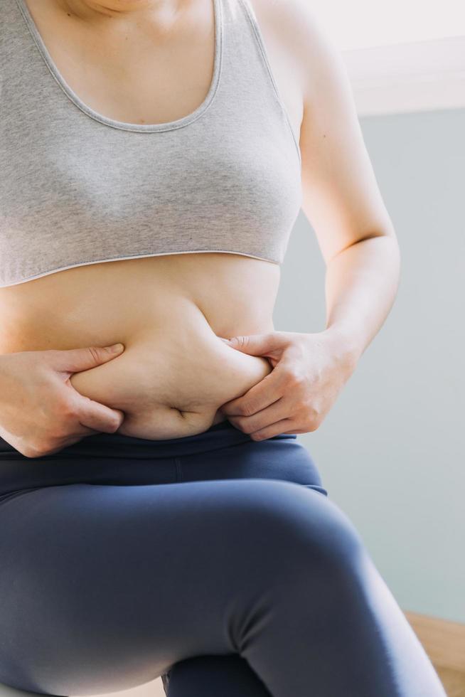 hermosa mujer gorda con cinta métrica usa su mano para exprimir el exceso de grasa que está aislado en un fondo blanco. ella quiere perder peso, el concepto de cirugía y descomponer grasa bajo el foto