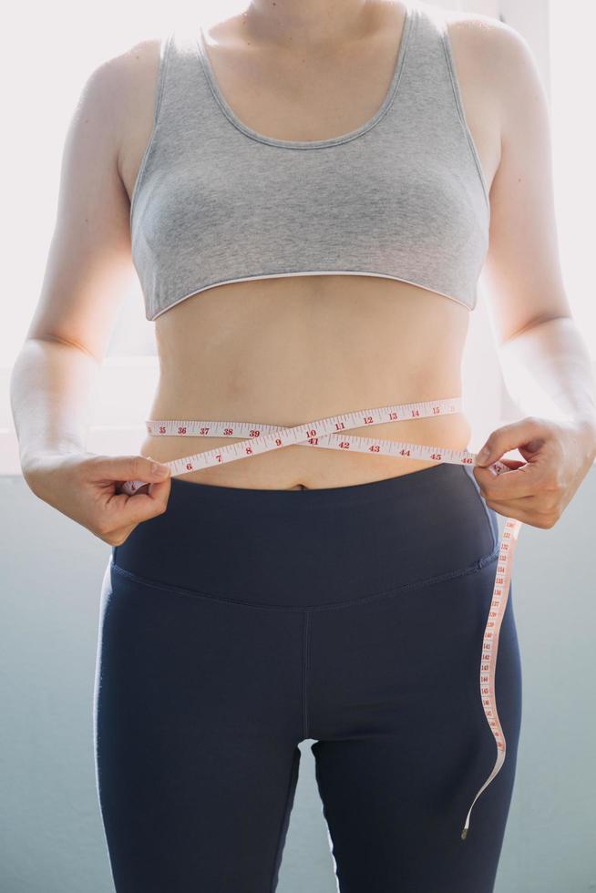 hermosa mujer gorda con cinta métrica usa su mano para exprimir el exceso de grasa que está aislado en un fondo blanco. ella quiere perder peso, el concepto de cirugía y descomponer grasa bajo el foto