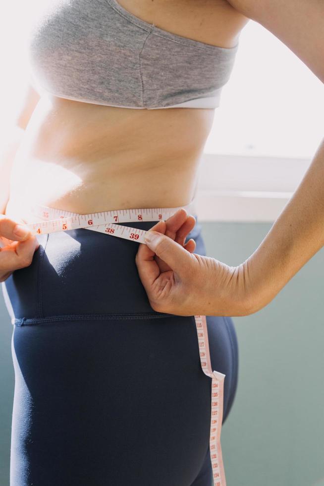 hermosa mujer gorda con cinta métrica usa su mano para exprimir el exceso de grasa que está aislado en un fondo blanco. ella quiere perder peso, el concepto de cirugía y descomponer grasa bajo el foto