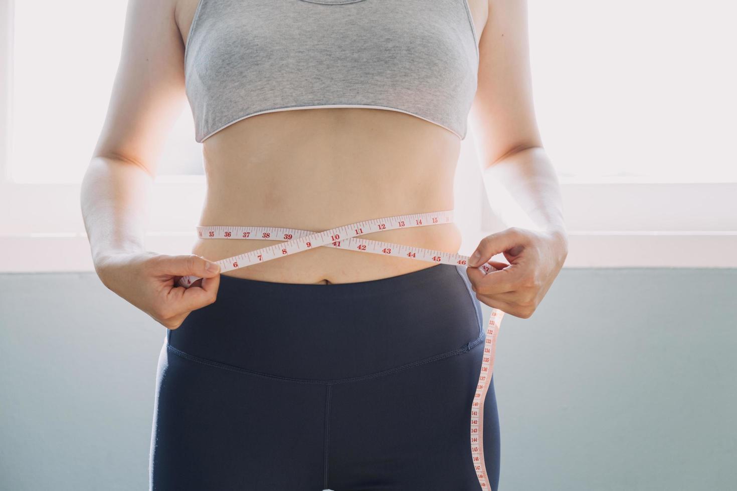 hermosa mujer gorda con cinta métrica usa su mano para exprimir el exceso de grasa que está aislado en un fondo blanco. ella quiere perder peso, el concepto de cirugía y descomponer grasa bajo el foto