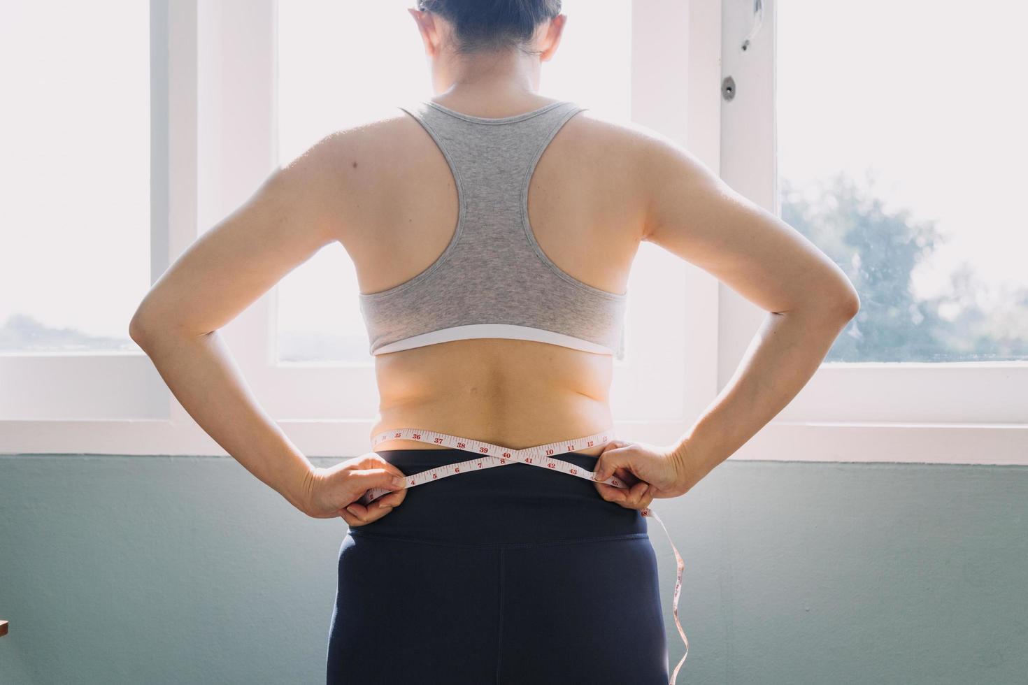 hermosa mujer gorda con cinta métrica usa su mano para exprimir el exceso de grasa que está aislado en un fondo blanco. ella quiere perder peso, el concepto de cirugía y descomponer grasa bajo el foto