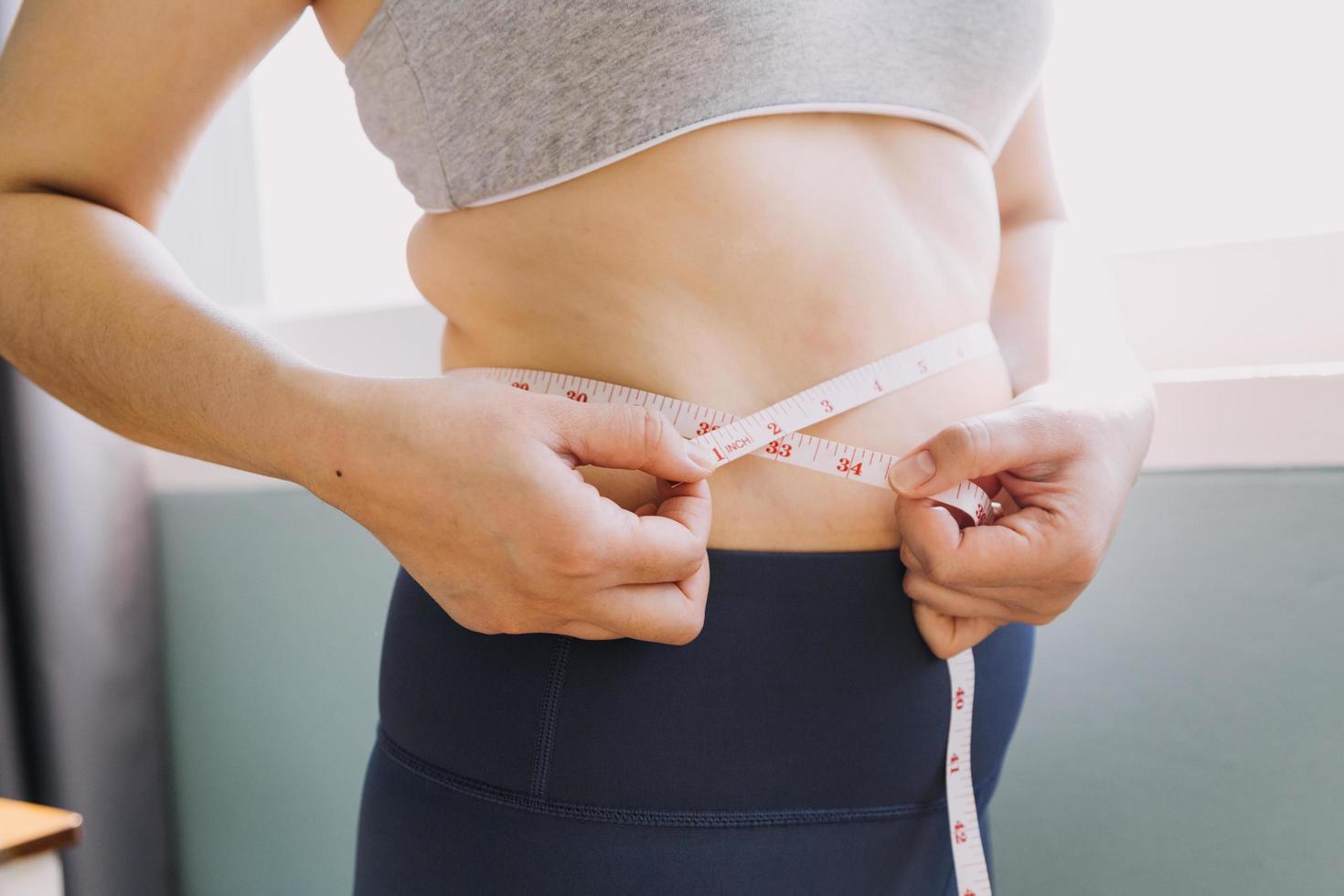 hermosa mujer gorda con cinta métrica usa su mano para exprimir el exceso de grasa que está aislado en un fondo blanco. ella quiere perder peso, el concepto de cirugía y descomponer grasa bajo el foto