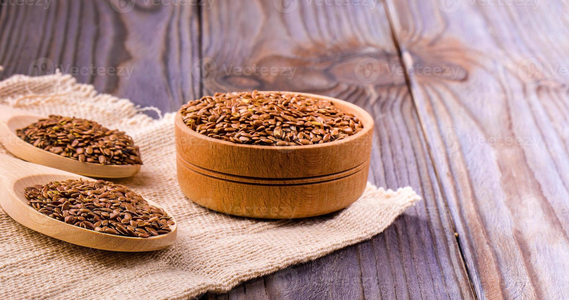 Brown flax seeds or flax seed in a small bowl on sacking and two wooden false on wooden table photo