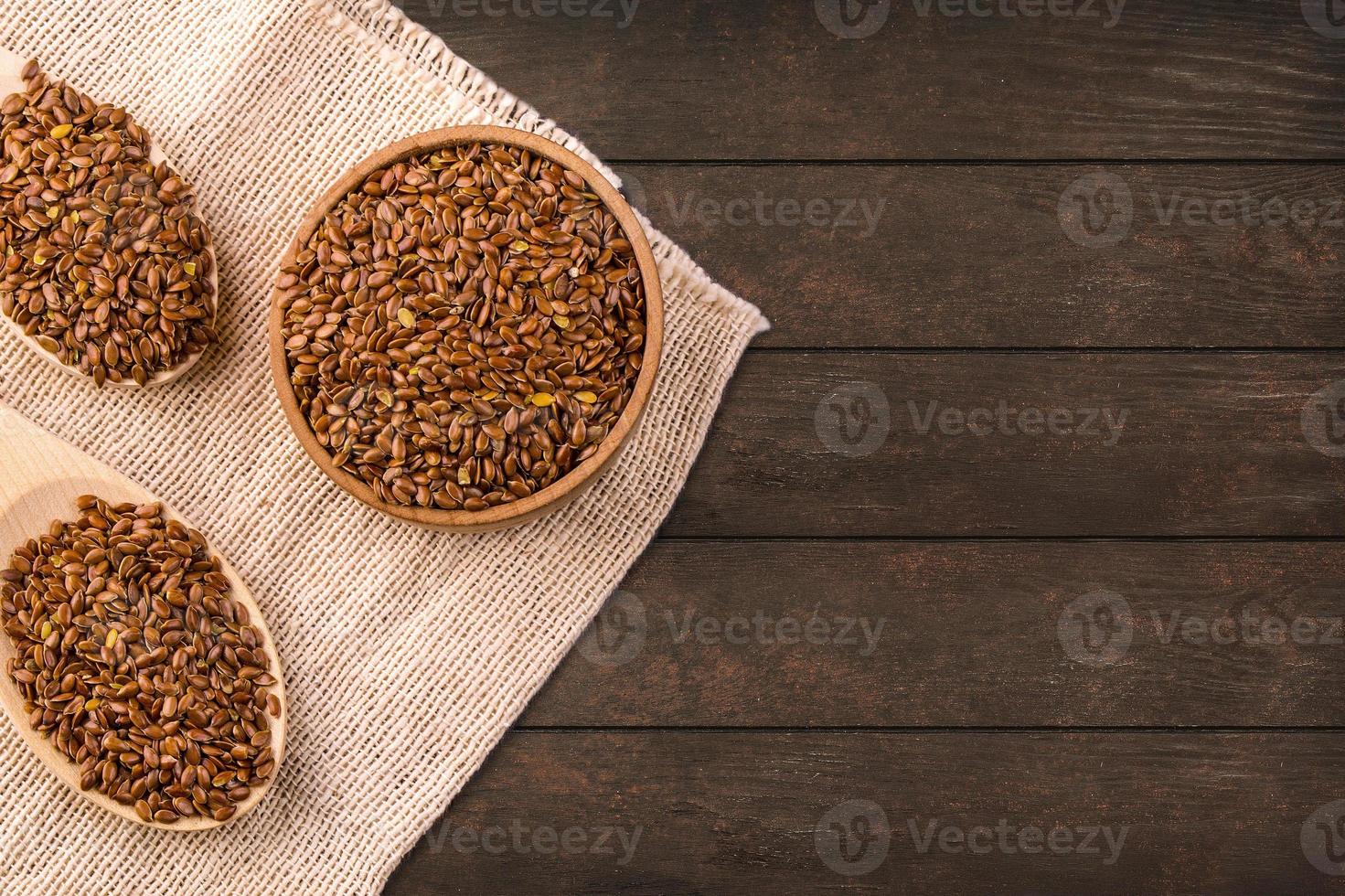 Brown flax seeds or flax seed in a small bowl on sacking and two wooden false on a brown wooden table photographed from above photo