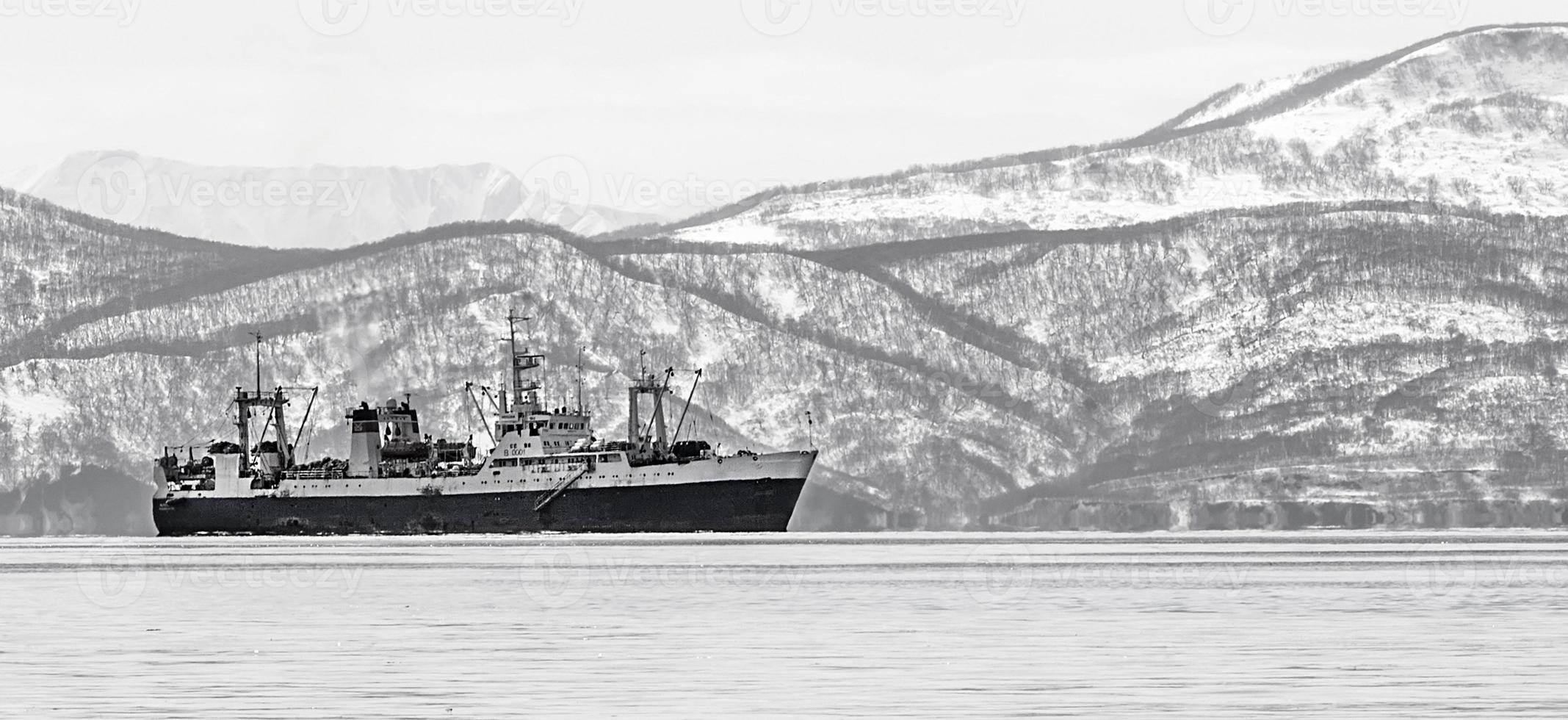 large fishing vessel on the background of snow-covered hills and volcanoes photo