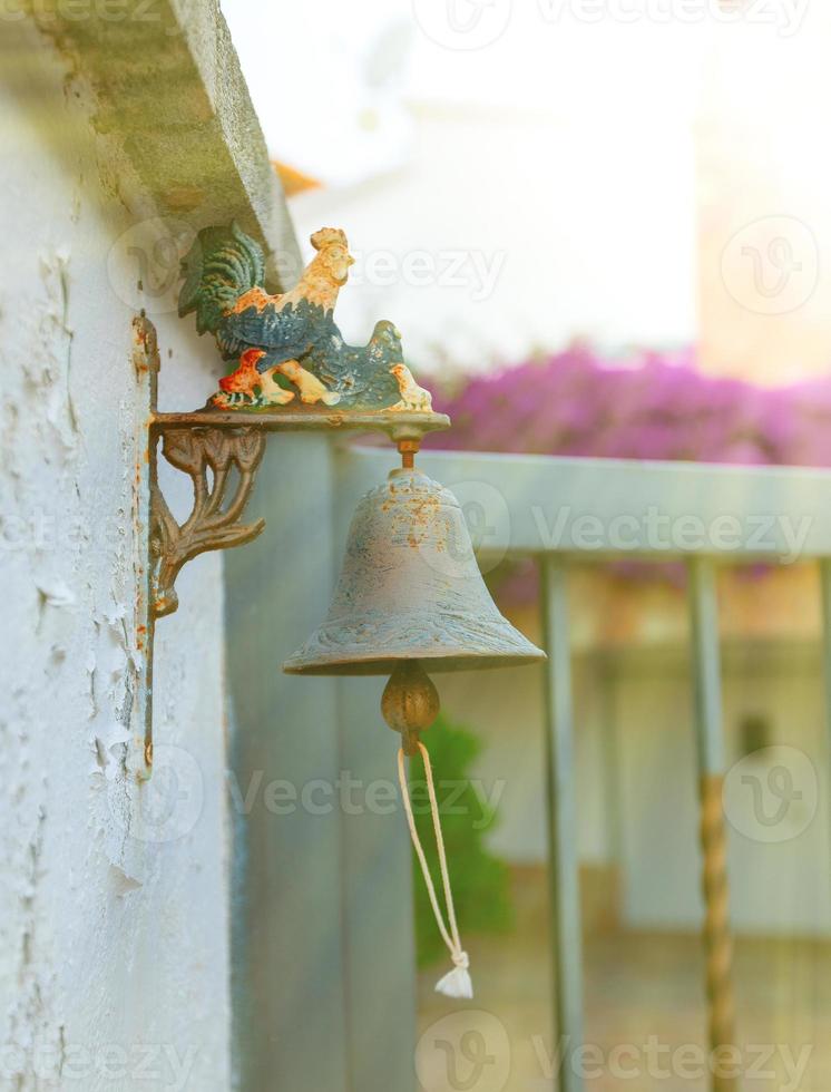 Small iron bell with colored rooster outside the house. photo