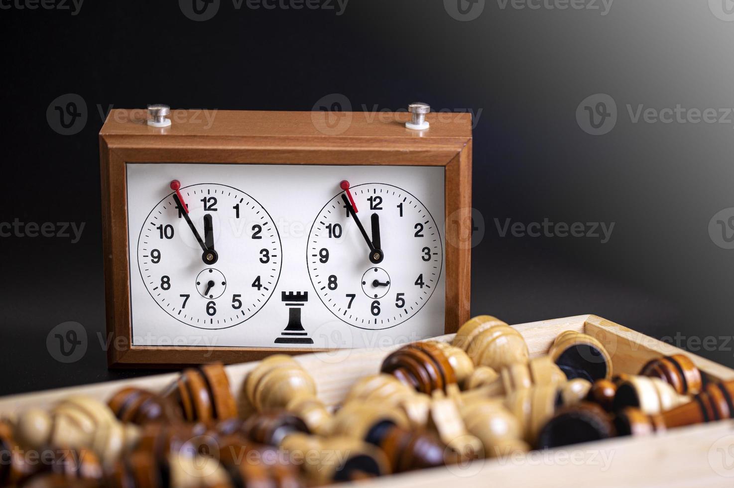 Chess pieces on a board and a chess clock on a dark background photo