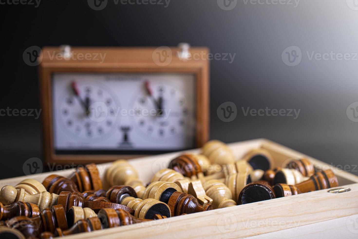 Chess pieces on a board and a chess clock on a dark background photo