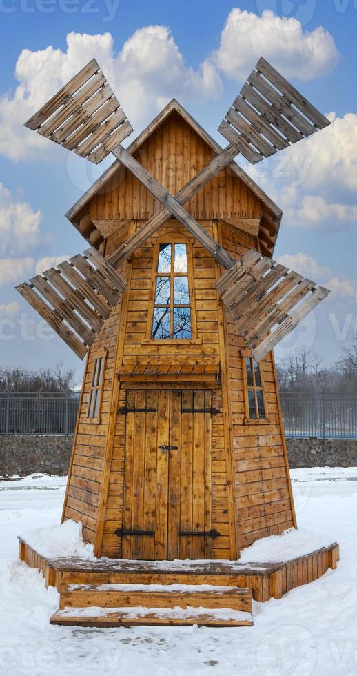 wooden windmill in winter on a background of blue sky with clouds photo