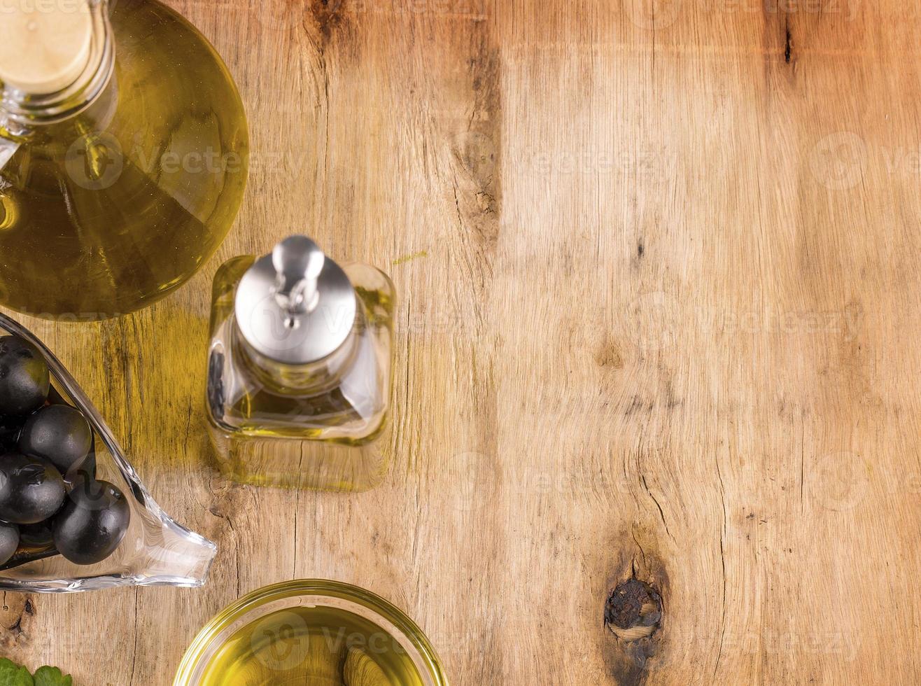 Olive oil with fresh herbs and Black olives on wooden photo