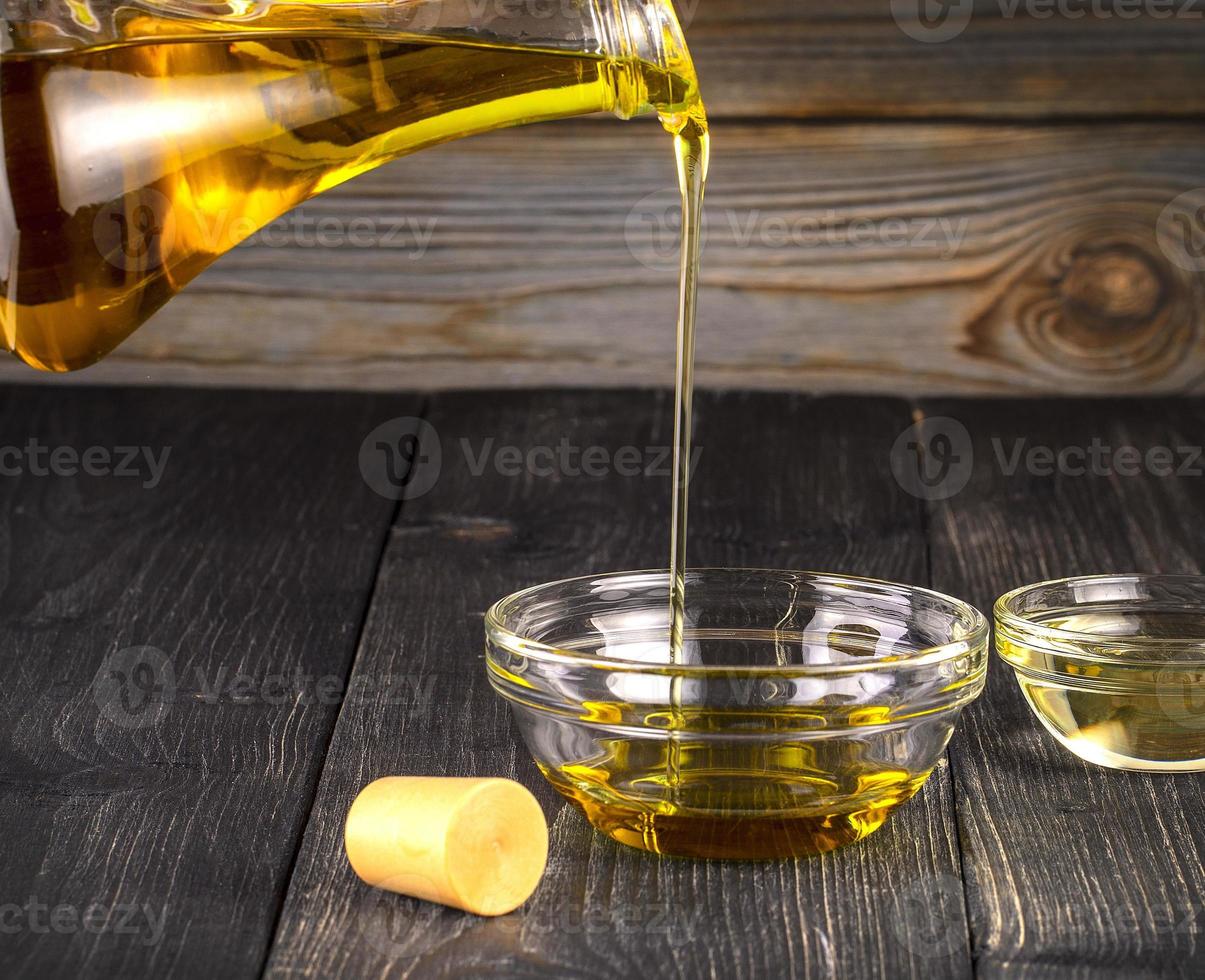 Pouring cooking oil a small glass cup on old wooden table photo