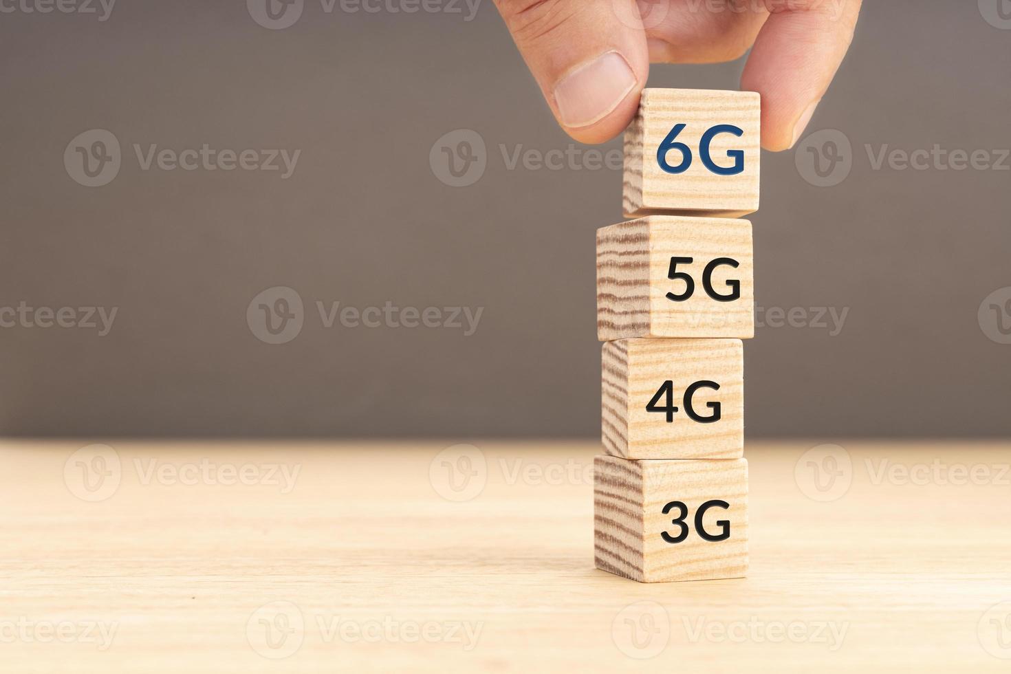 6G network connecting technology concept. Hand placing a 6G cube on top of other stacked blocks with older communication technologies. Copy space photo