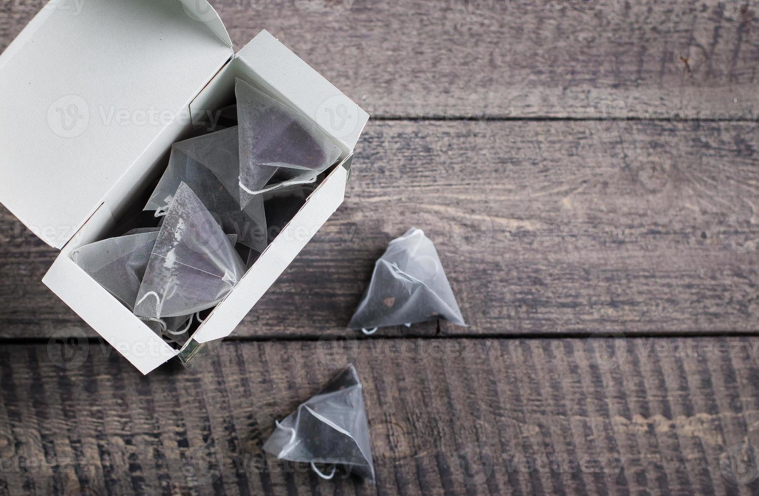 Tea bag shape of pyramid in paper packaging box on wooden table background. Top view with copy space photo