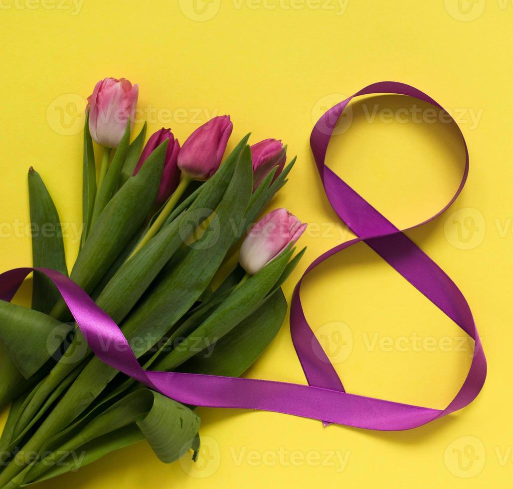 Beautiful spring tulips and ribbon eight shaped on yellow background. Concept of Valentines day, Women's Day March eight, Mothers day. photo