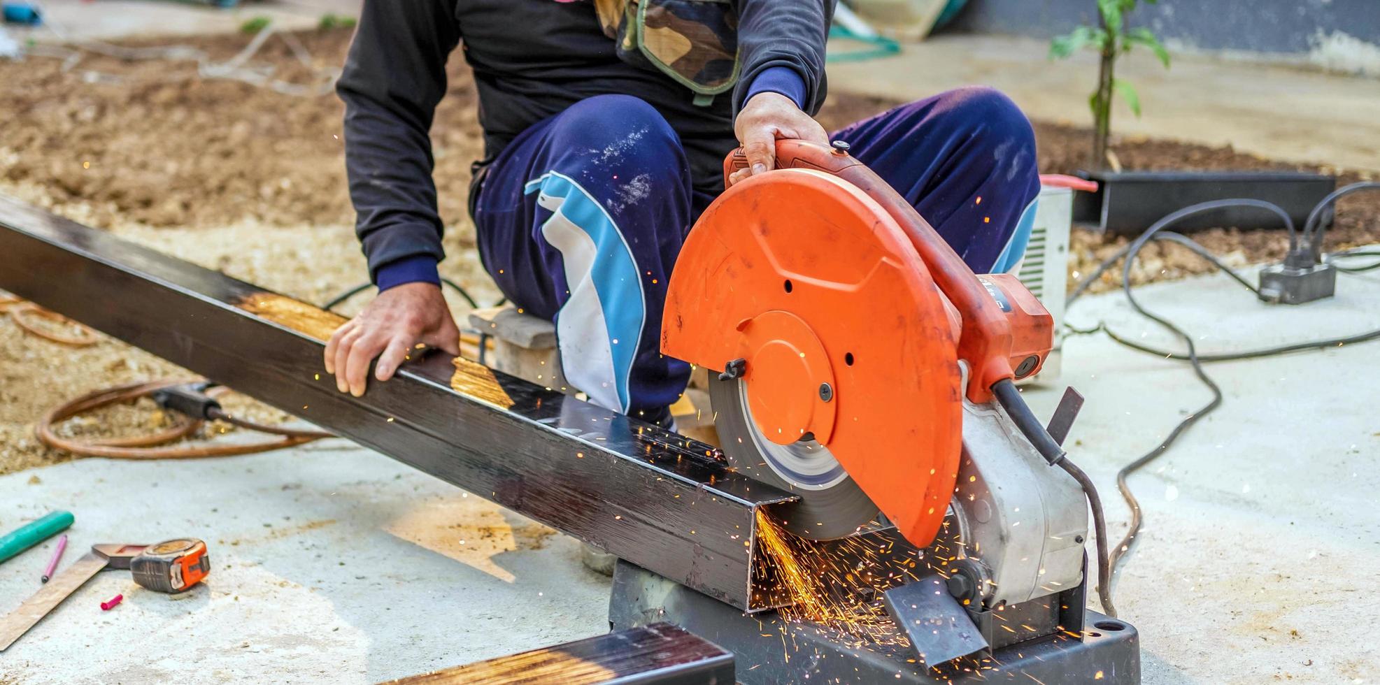 el trabajador en la ropa de trabajo utiliza un cortador de acero eléctrico. cortar grandes barras de acero en el sitio de construcción foto