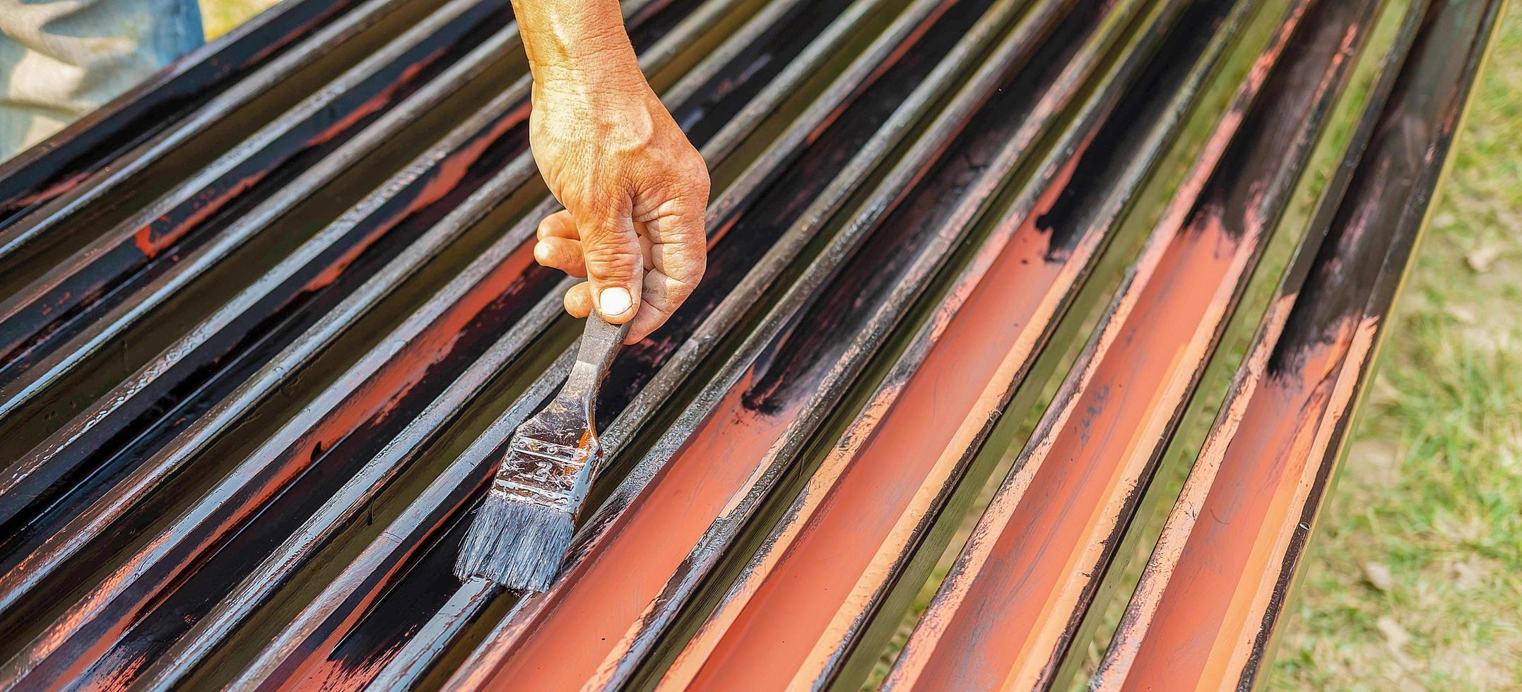 primer plano de la mano del trabajador de un pintor sosteniendo una trama de pintura trabajando pintura negra en una pila de barras de hierro. foto