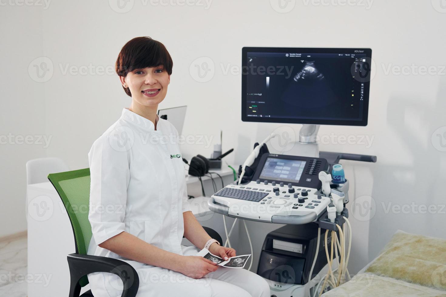 Portrait of obstetric doctor that sits in the clinic room with ultrasound device photo