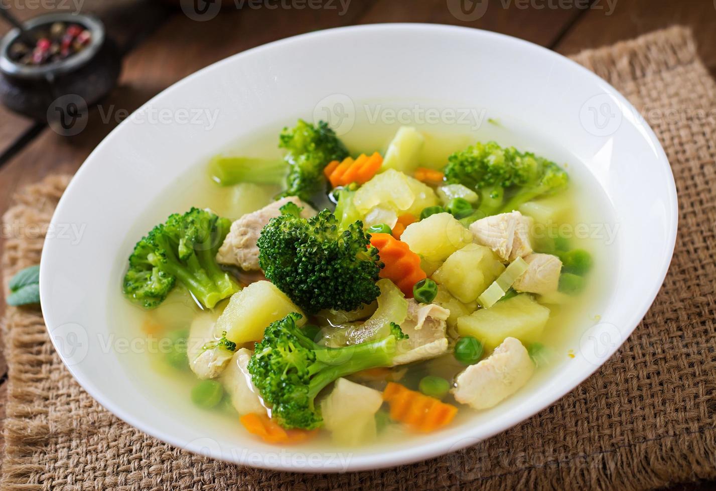 Chicken soup with broccoli, green peas, carrots and celery in a white bowl on a wooden background in rustic style photo