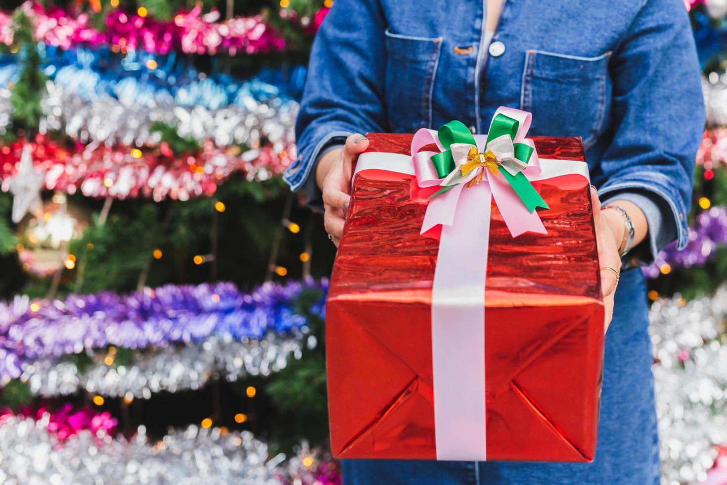 Woman holding present in a red box on the background of Christmas tree. photo