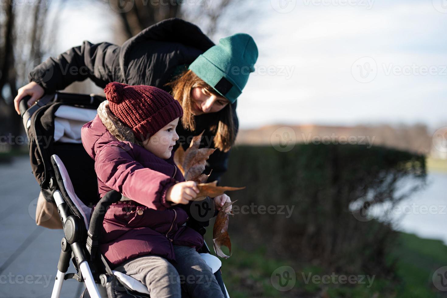 Young woman in city park with baby stroller. Warm autumn weather for outdoor activity. photo