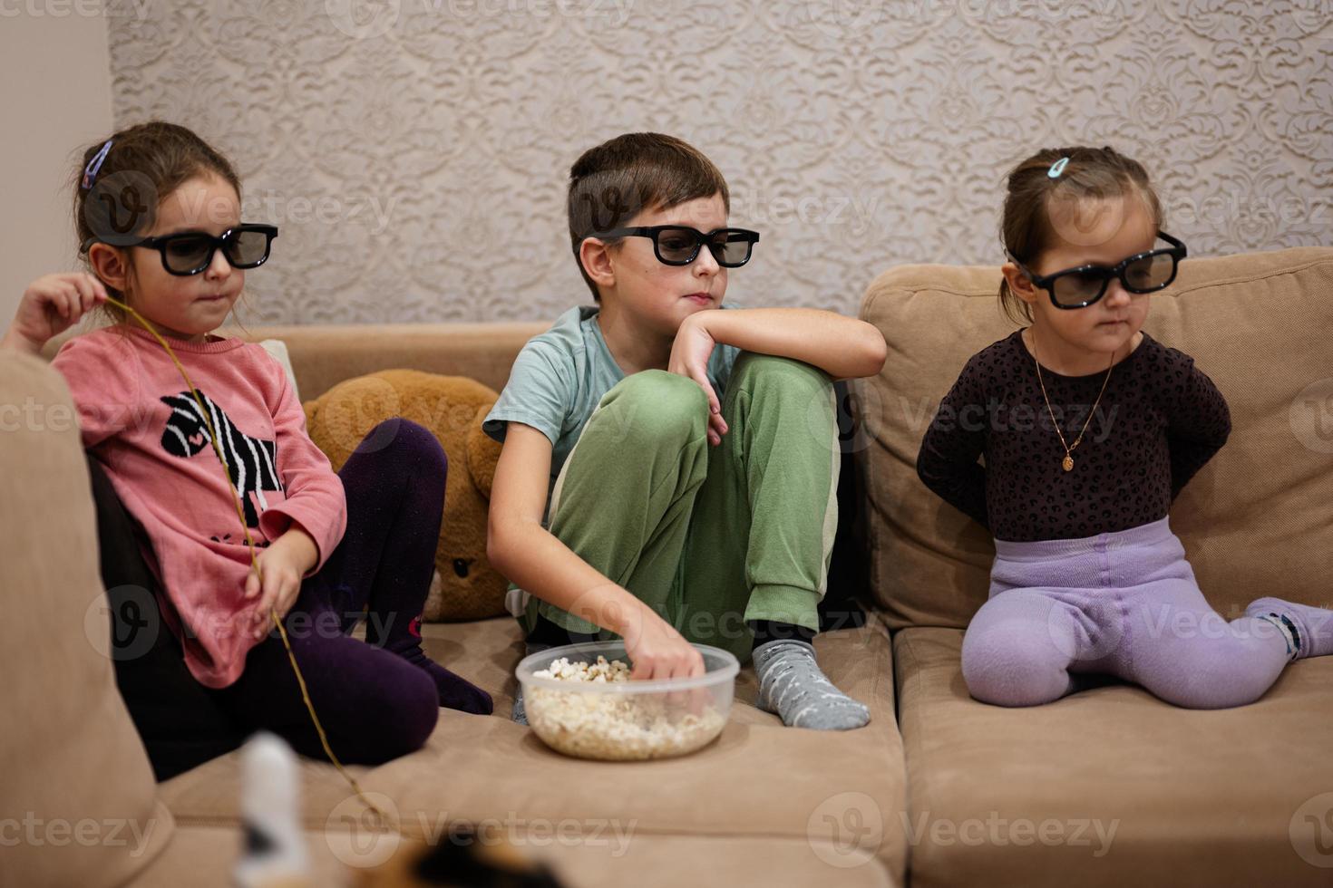 tres niños sentados en la sala de estar, usan gafas 3d viendo películas o dibujos animados. foto