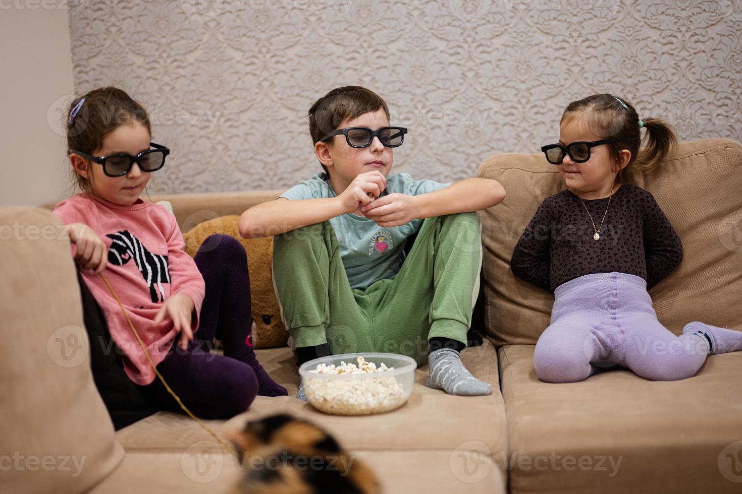 tres niños sentados en la sala de estar, usan gafas 3d viendo películas o dibujos animados. foto