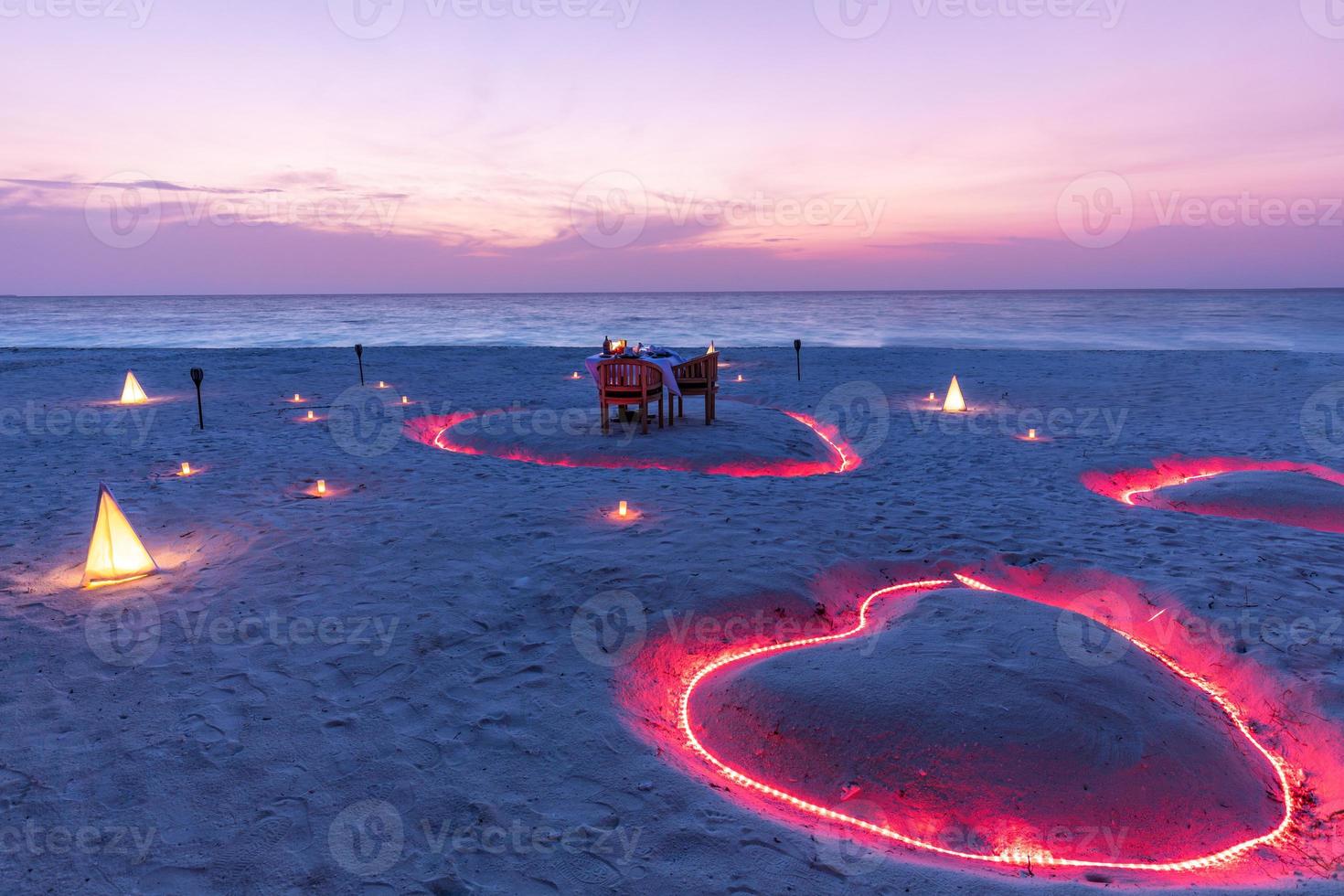 una pareja joven comparte una cena romántica con velas en forma de corazón cerca de la playa de arena del mar. hermoso destino de luna de miel, viajes de lujo, cena exótica en la playa al atardecer con fondo marino foto