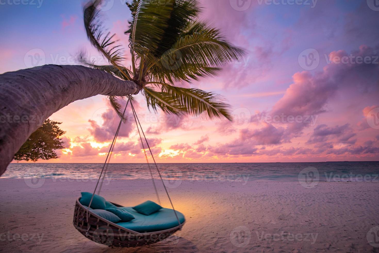 Romantic beach sunset. Palm tree with swing hanging before majestic clouds sky. Dream nature landscape, tropical island paradise, couple destination. Love coast, closeup sea sand. Relax pristine beach photo