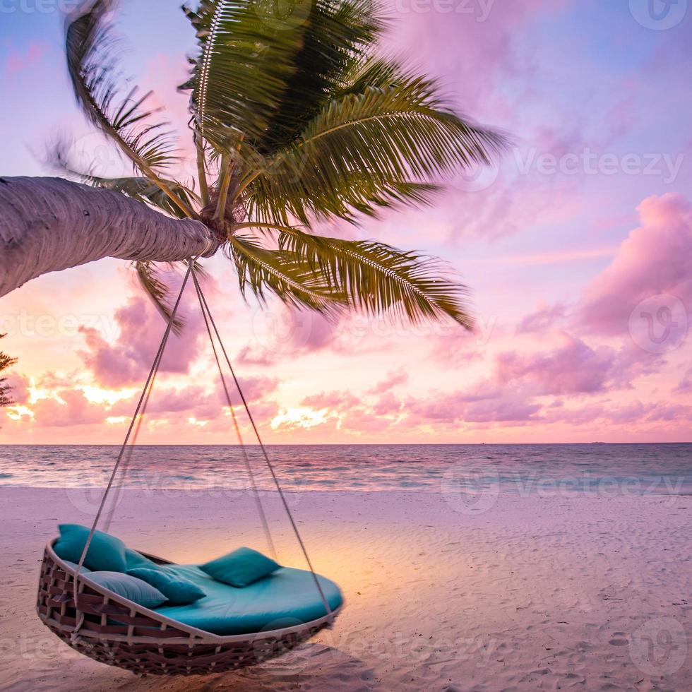 Square format. Tropical beach sunset landscape with beach swing or hammock and sunset sky white sand and calm sea for beach banner. Perfect beach scene vacation and summer holiday concept photo