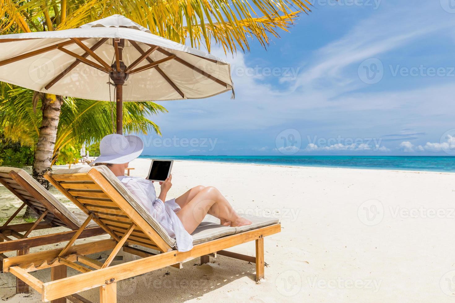 Young woman in hat with tablet pc at the beach. Perfect tranquil beach scenery, relaxed woman working as home office. Wonderful nature scenery in tropical beach. Copy space for text, sunny summer photo
